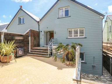 An outdoor patio area with steps leading to a blue house featuring windows and a door at Harmon Vale in Solva