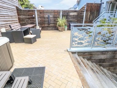 An outdoor patio with wicker furniture wooden stairs potted plants and a metal railing with fish designs at Harmon Vale in Solva
