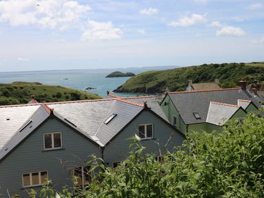 Houses with slate roofs overlooking a coastal landscape with green hills and ocean at Harmon Vale in Solva