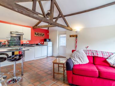 A kitchen and living area with wooden beams white cabinets red wall and red sofa at The Nest Box in Diss