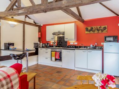 A kitchen with white cabinets a red wall black tiles and wooden beams at The Nest Box in Diss