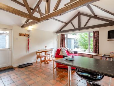 A living space with a red sofa near a window dining table with two chairs and exposed wooden ceiling beams at The Nest Box in Diss
