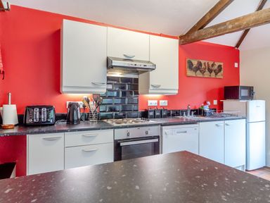 A kitchen with white cabinets black appliances and red walls at The Nest Box in Diss