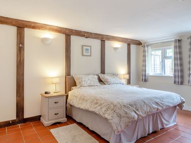 A bedroom with a double bed two bedside tables with lamps a window with curtains and wooden beams on the walls at The Nest Box in Diss