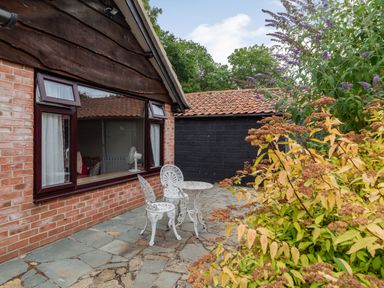 A patio area with two white metal chairs and a table next to a brick house with a large window and plants at The Nest Box in Diss