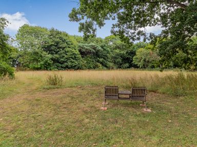 A wooden bench with a small table in front of a grassy field with trees in the background at The Nest Box in Diss