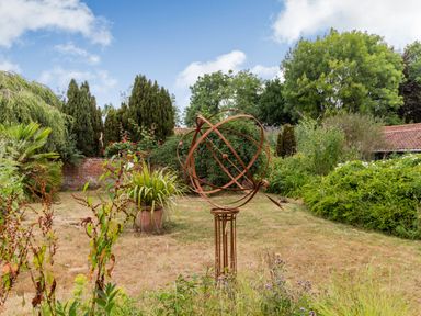 A garden with a metal sculpture surrounded by various plants and trees at The Nest Box in Diss