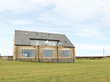 A stone house with large windows and a slate roof on a grassy field at St Dolmen in Embleton