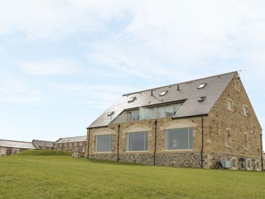 A stone building with large windows and a slate roof on a grassy hill at St Dolmen in Embleton