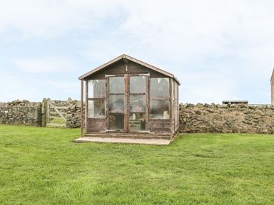 A wooden garden shed with glass doors on a grassy lawn near a stone wall at St Dolmen in Embleton
