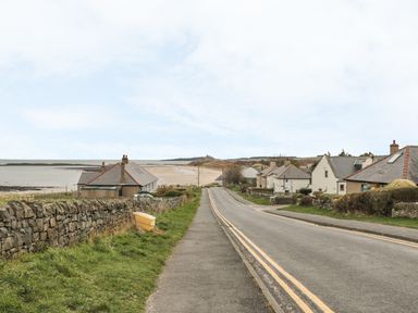A paved road with houses on the right and a stone wall on the left leading to a beach at St Dolmen in Embleton