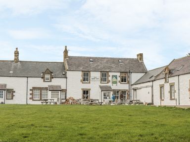 An exterior view of a white building with multiple chimneys and windows with a grassy area in front at St Dolmen in Embleton