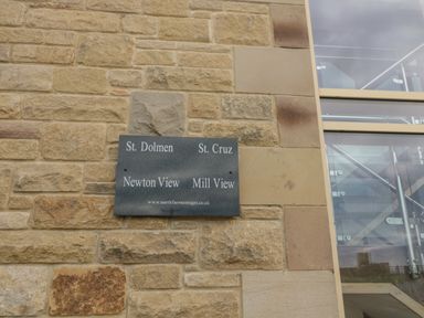 A stone wall with a sign listing St Dolmen St Cruz Newton View and Mill View next to a glass and metal staircase at St Dolmen in Embleton