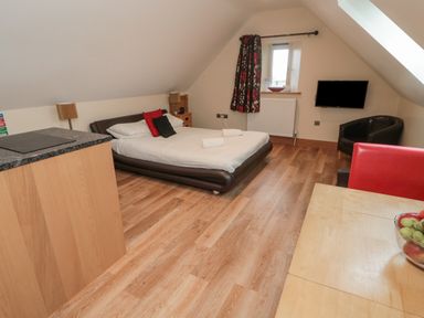 A bedroom with a bed a small wooden cupboard a wall-mounted television a black chair and a table with a fruit bowl at St Dolmen in Embleton