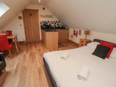 A bedroom with a bed towels bedside table kitchenette dining table with chairs and wooden flooring at St Dolmen in Embleton