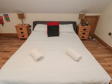 A bed with white sheets two rolled towels and two cushions between wooden bedside tables with lamps at St Dolmen in Embleton