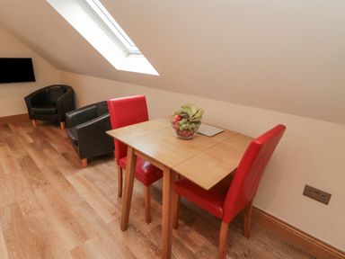 A dining table with red chairs and a bowl of fruit under a skylight with two black armchairs in the corner at St Dolmen in Embleton