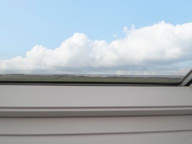 A window view of a flat landscape with green fields and cloudy sky at St Dolmen in Embleton