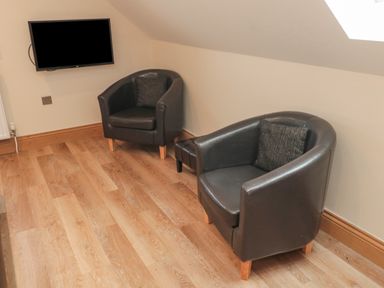 A room with two black leather armchairs each with a cushion a small black ottoman wooden floor and a wall-mounted television at St Dolmen in Embleton