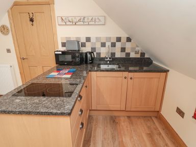 A kitchen with wooden cabinets granite countertop microwave toaster kettle and a sink at St Dolmen in Embleton