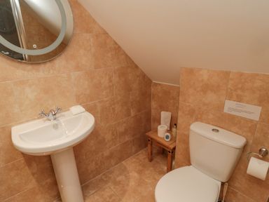 A small bathroom with a pedestal sink mirror toilet and a wooden stool with toiletries at St Dolmen in Embleton
