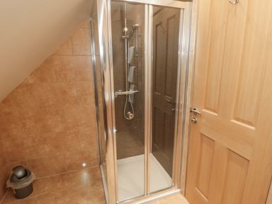 A bathroom with a glass shower enclosure a tiled wall a wooden door and a small trash bin at St Dolmen in Embleton