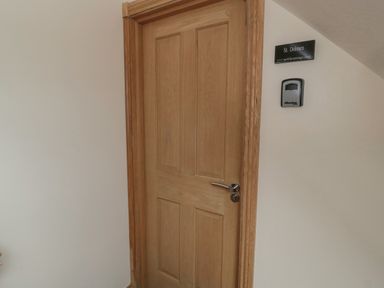 A wooden door with a silver handle and a sign reading St Dolmen on a white wall at St Dolmen in Embleton