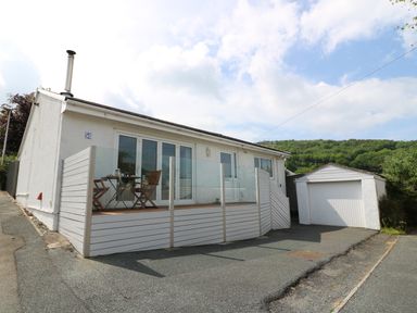 A white house with a glass fenced patio and wooden furniture next to a detached garage at 54 The Moorings in St Dogmaels