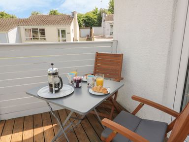 A small balcony with a table set for breakfast with coffee, croissants, jam, orange juice and wooden chairs at 54 The Moorings in St Dogmaels