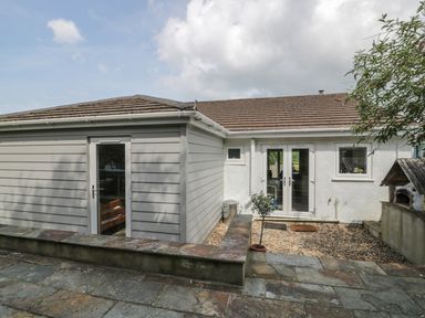 An outdoor area with stone paving a small tree a gravel section and a building with white walls and grey siding and two doors at 54 The Moorings in St Dogmaels