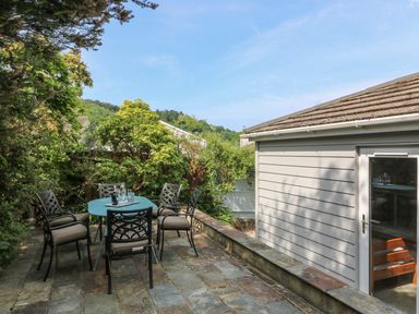 An outdoor patio area with a table and six chairs surrounded by greenery at 54 The Moorings in St Dogmaels