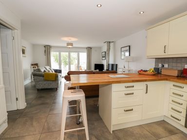 An open kitchen and living room with cream cabinets wooden countertop stools and sofas with large glass doors in the background at 54 The Moorings in St Dogmaels