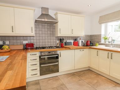 A kitchen with cream cabinets a wooden countertop a gas stove an oven a red kettle and a window with a blind at 54 The Moorings in St Dogmaels