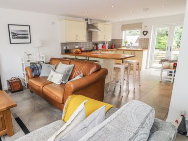 A kitchen with cream cabinets and wooden countertops next to a living area with a brown leather sofa and a patterned sofa at 54 The Moorings in St Dogmaels