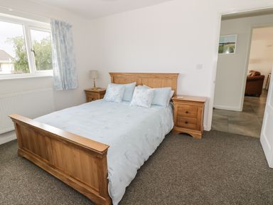 A bedroom with a wooden bed and matching bedside tables with a lamp and window at 54 The Moorings in St Dogmaels