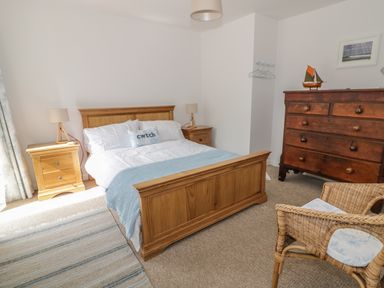 A bedroom with a wooden bed frame bedside tables two lamps a wooden dresser a wicker chair and a rug at 54 The Moorings in St Dogmaels