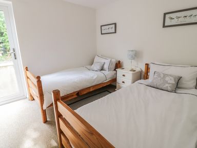 A bedroom with two single beds with white bedding and a small white nightstand with a lamp at 54 The Moorings in St Dogmaels