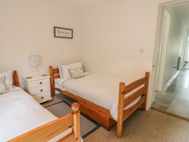 A bedroom with two single wooden beds a white nightstand with a lamp and a framed picture above the bed at 54 The Moorings in St Dogmaels