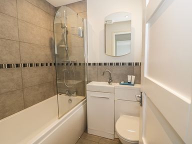 A bathroom with a bathtub shower combination a sink with a cabinet and a toilet at 54 The Moorings in St Dogmaels