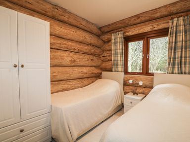 A bedroom with two single beds a small white nightstand a double door wardrobe and a window with curtains at Moorhen Lodge in North Kessock