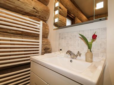 A bathroom sink with a faucet a towel and a flower in a vase and a white towel radiator against a log wall at Moorhen Lodge in North Kessock