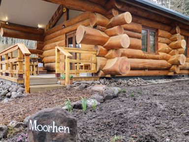A wooden log cabin with a small porch and railing and a rock with Moorhen written on it at Moorhen Lodge in North Kessock