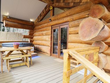 A wooden deck with picnic table and hot tub outside a log cabin at Moorhen Lodge in North Kessock
