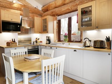 A kitchen with wooden cabinets and table four white chairs a microwave oven kettle toaster and a window with a flower pot at Moorhen Lodge in North Kessock