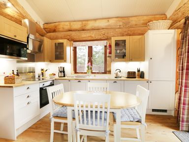 A kitchen with wooden beams a dining table with chairs and kitchen appliances at Moorhen Lodge in North Kessock