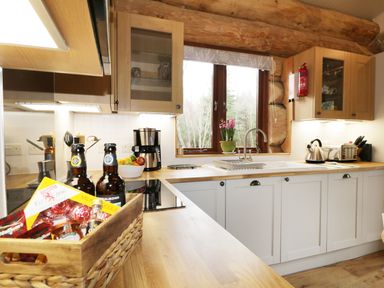 A kitchen with wooden countertops white cabinets bottles and snacks on the counter a window with a plant and a sink at Moorhen Lodge in North Kessock