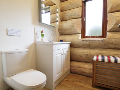 A bathroom with a toilet, white sink cabinet, wooden walls, window, and a striped cushioned bench at Moorhen Lodge in North Kessock