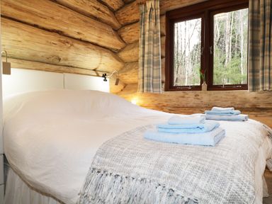 A bedroom with a made bed folded towels on the blanket wooden log walls and a window with curtains at Moorhen Lodge in North Kessock