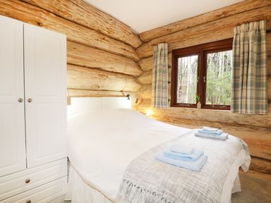 A bedroom with a bed covered in white linens and blue towels on a gray throw next to a white wardrobe and a window with plaid curtains at Moorhen Lodge in North Kessock