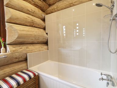 A bathroom with a bathtub shower combination a wooden log wall and a striped bench at Moorhen Lodge in North Kessock